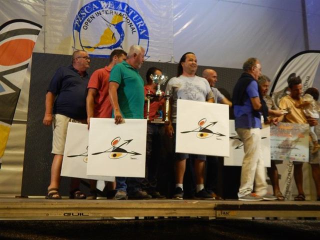 Grupo de personas sobre un escenario con una copa y carteles blancos, bajo el cartel del Open Internacional de Pesca de Altura
