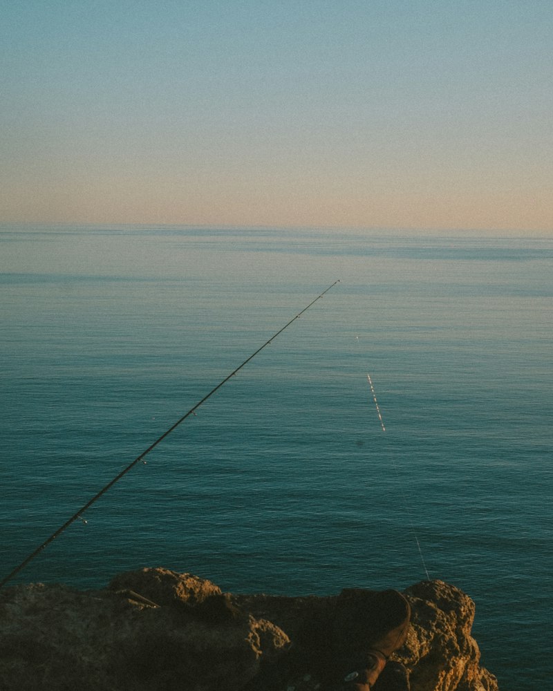 Caña de pesca extendida sobre el mar en calma al amanecer desde unas rocas