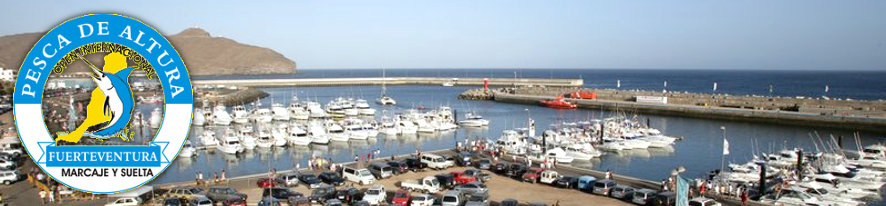 Puerto con numerosas embarcaciones amarradas y, a la izquierda, el logotipo «Pesca de altura Fuerteventura, marcaje y suelta»